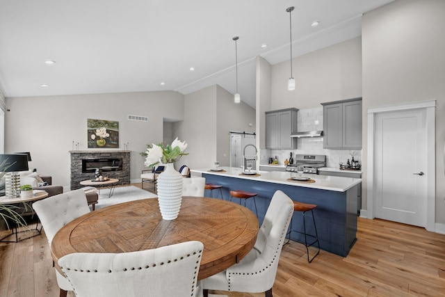 dining space with light wood finished floors, high vaulted ceiling, a stone fireplace, recessed lighting, and visible vents