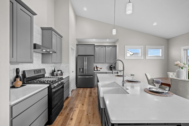 kitchen featuring a kitchen island with sink, backsplash, appliances with stainless steel finishes, vaulted ceiling, and gray cabinetry