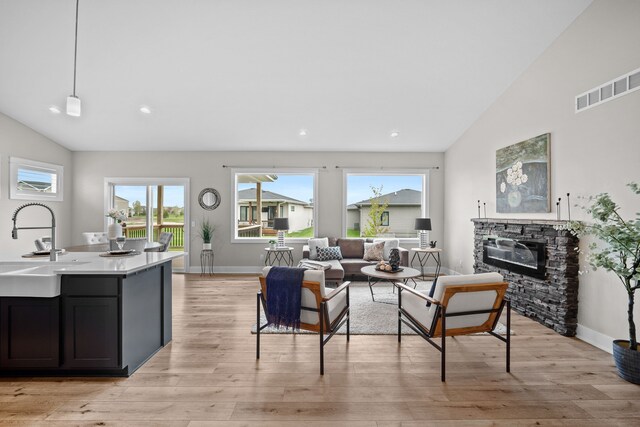 living area with visible vents, a fireplace, baseboards, light wood-type flooring, and vaulted ceiling