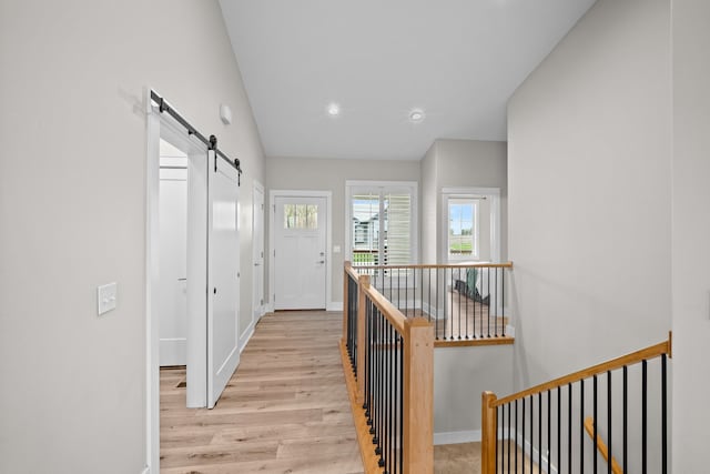 hallway featuring baseboards, light wood-style floors, recessed lighting, a barn door, and an upstairs landing