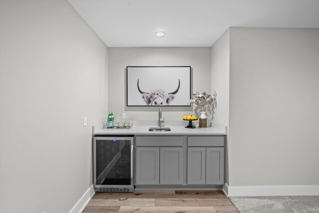bar with a sink, light wood-style floors, indoor wet bar, baseboards, and wine cooler