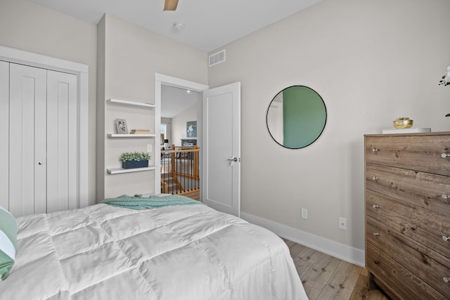 bedroom with ceiling fan, visible vents, wood finished floors, baseboards, and a closet