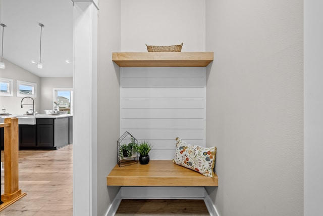 mudroom with light wood-style floors, baseboards, vaulted ceiling, and a sink