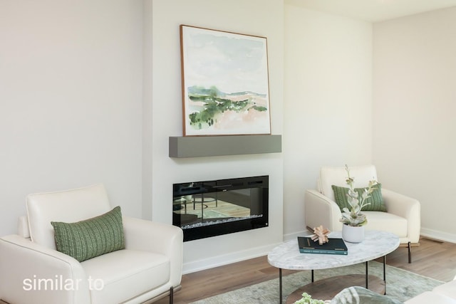 sitting room featuring a glass covered fireplace, baseboards, and wood finished floors