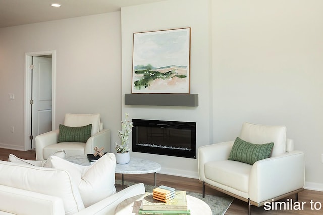 living room featuring a glass covered fireplace, recessed lighting, baseboards, and wood finished floors