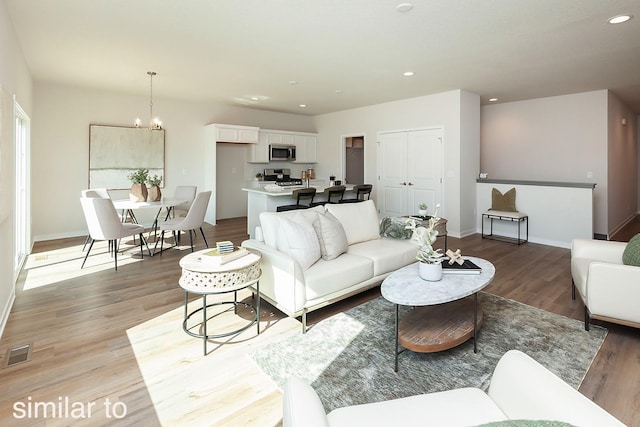 living room with light wood-type flooring, visible vents, recessed lighting, an inviting chandelier, and baseboards