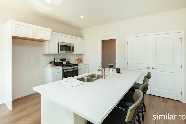 kitchen featuring light wood finished floors, a sink, stainless steel appliances, white cabinetry, and backsplash