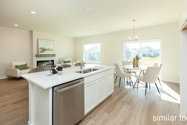 kitchen with light wood-style flooring, a sink, a glass covered fireplace, white cabinetry, and dishwasher