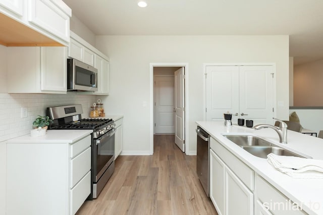 kitchen with a sink, tasteful backsplash, light wood-style floors, appliances with stainless steel finishes, and light countertops