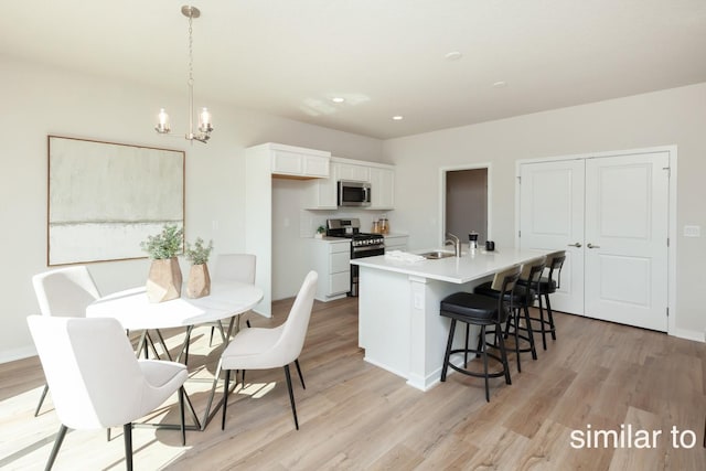 kitchen with a center island with sink, a sink, stainless steel appliances, white cabinets, and light wood finished floors