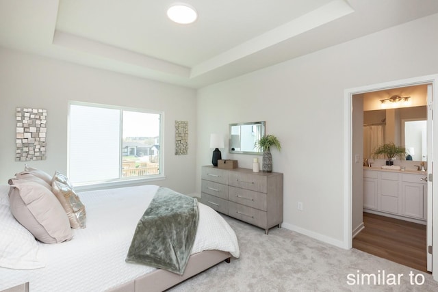 bedroom with baseboards, light colored carpet, connected bathroom, and a tray ceiling