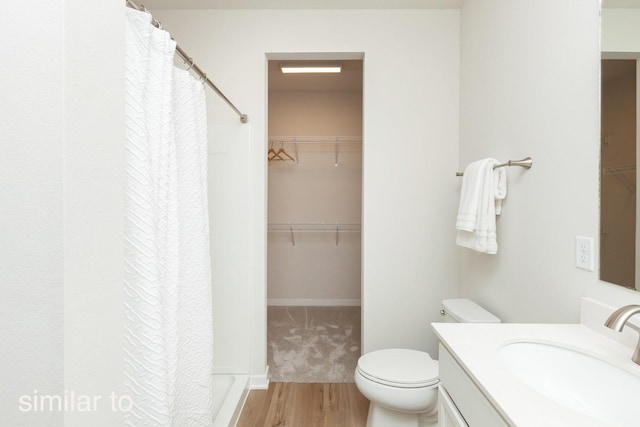 full bath with a spacious closet, toilet, vanity, and wood finished floors