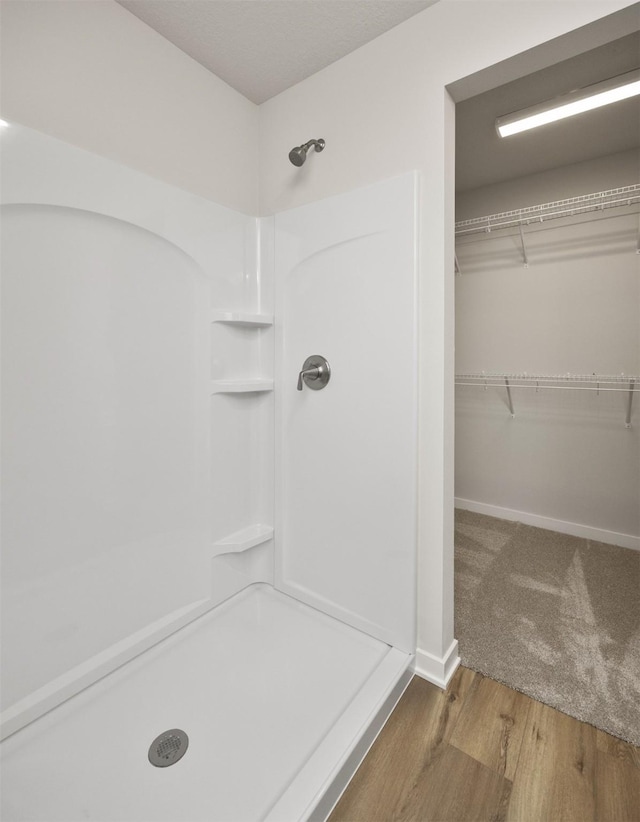 bathroom with a spacious closet, baseboards, wood finished floors, and a shower