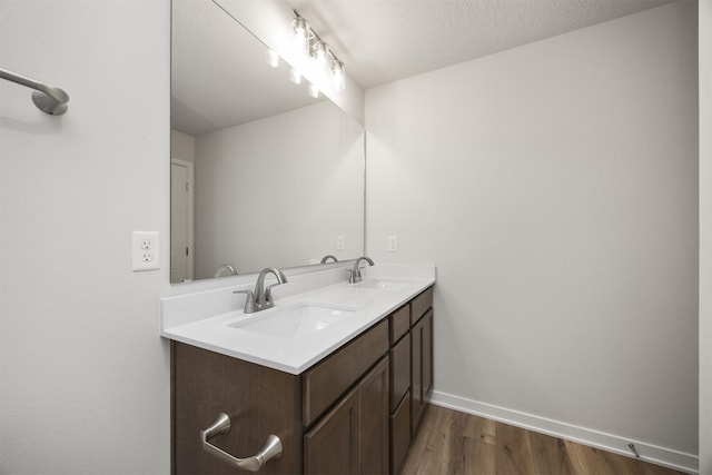 bathroom with baseboards, wood finished floors, a sink, and double vanity