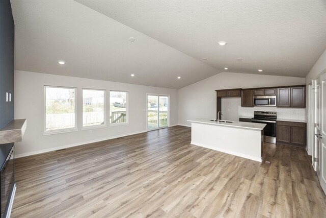 kitchen with stainless steel appliances, a sink, light wood-type flooring, open floor plan, and lofted ceiling