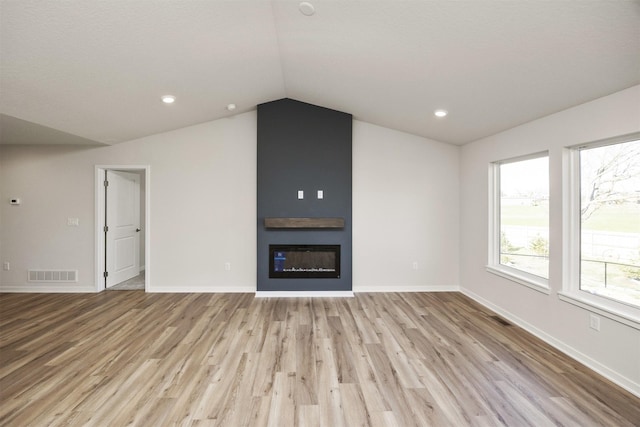unfurnished living room with lofted ceiling, a large fireplace, visible vents, and light wood-type flooring