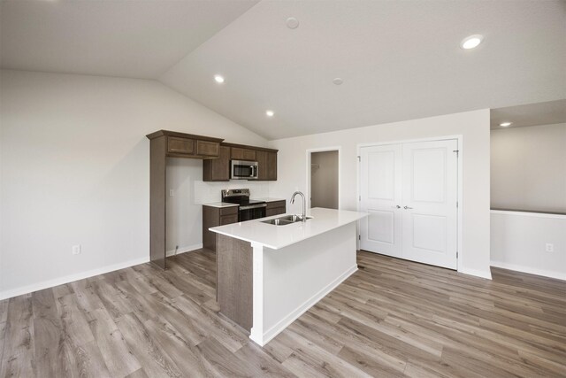 kitchen featuring stainless steel appliances, dark brown cabinets, a sink, light wood-style floors, and a center island with sink