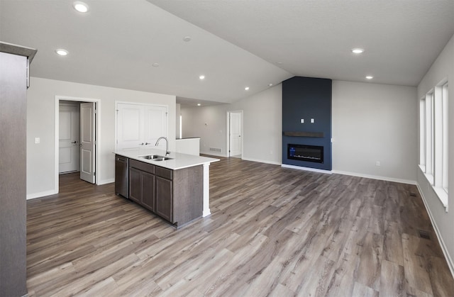 kitchen with light wood finished floors, stainless steel dishwasher, a sink, dark brown cabinets, and baseboards