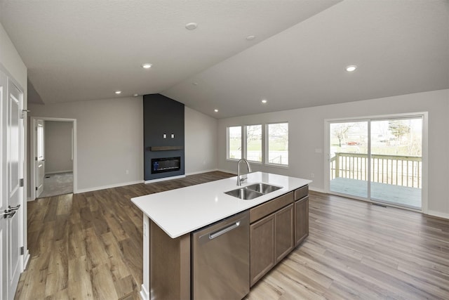 kitchen featuring open floor plan, light wood finished floors, stainless steel dishwasher, and a sink