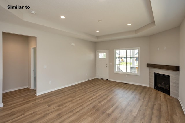 unfurnished living room featuring light wood-style floors, a raised ceiling, and baseboards