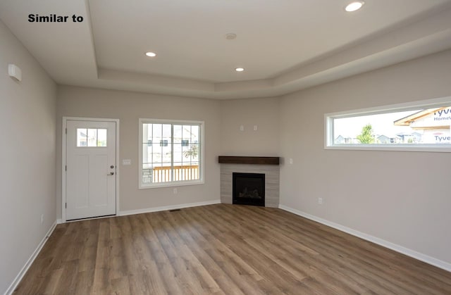 unfurnished living room with a tray ceiling, a healthy amount of sunlight, and baseboards