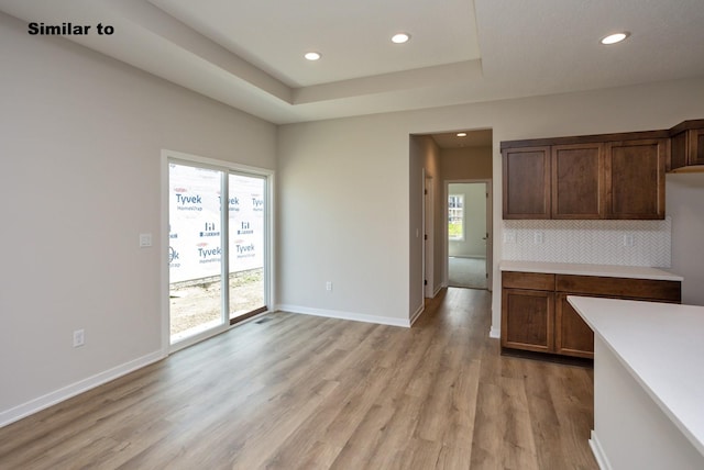 kitchen with light wood finished floors, a raised ceiling, light countertops, decorative backsplash, and baseboards