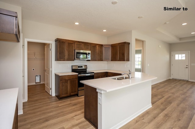 kitchen with stainless steel appliances, light countertops, backsplash, a sink, and light wood-type flooring