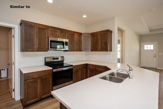 kitchen featuring a peninsula, stainless steel appliances, light countertops, light wood-type flooring, and a sink