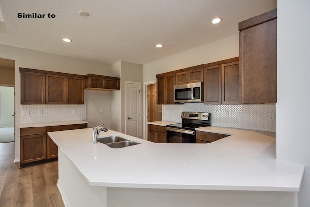 kitchen featuring stainless steel appliances, a peninsula, a sink, light countertops, and light wood-type flooring