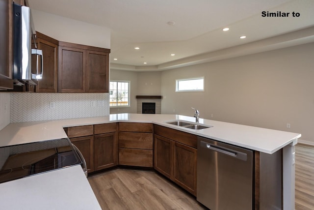 kitchen with light wood-style flooring, a peninsula, a sink, light countertops, and stainless steel dishwasher