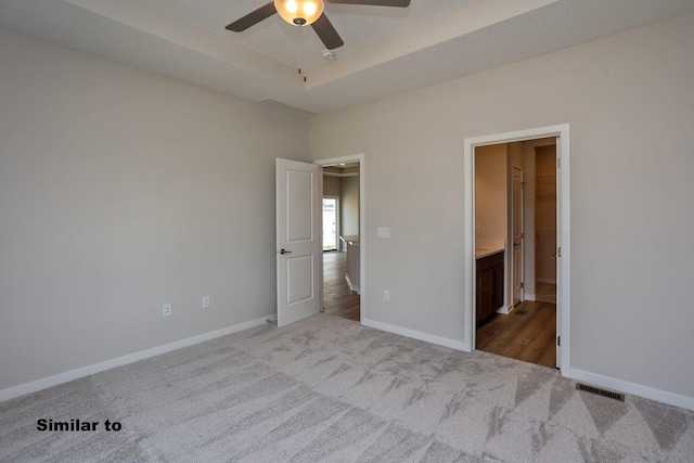 unfurnished bedroom featuring carpet floors, a raised ceiling, visible vents, ensuite bathroom, and baseboards