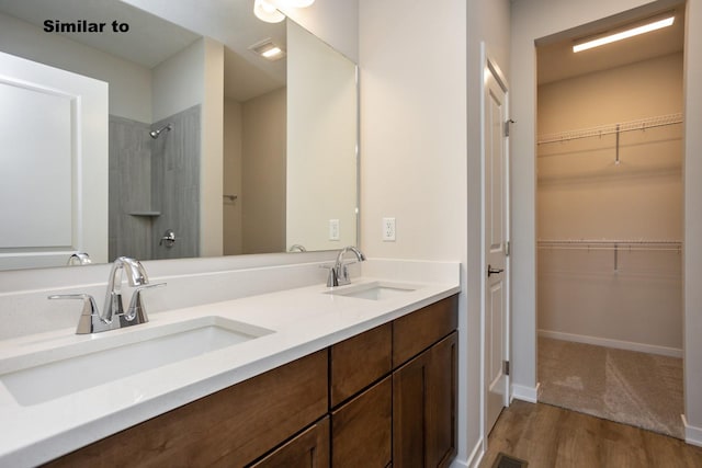 bathroom featuring double vanity, a sink, a spacious closet, and wood finished floors