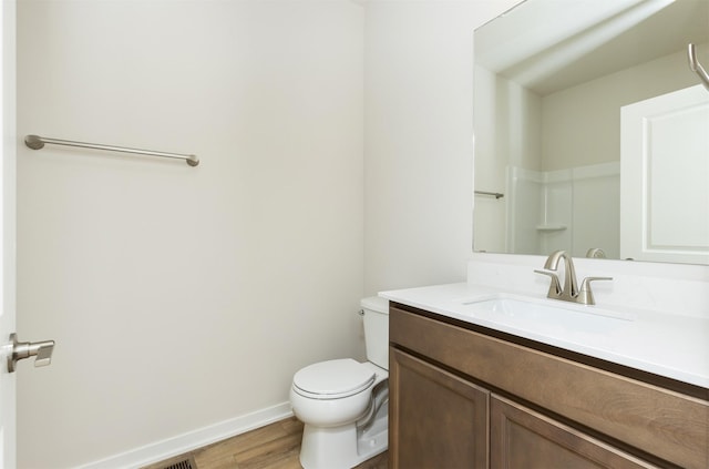 bathroom with toilet, vanity, wood finished floors, and baseboards