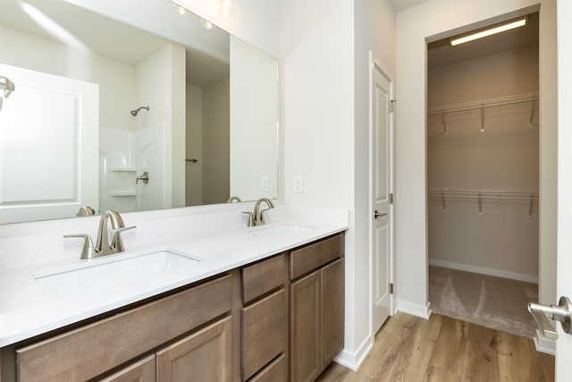 bathroom with a walk in closet, wood finished floors, a sink, and a shower