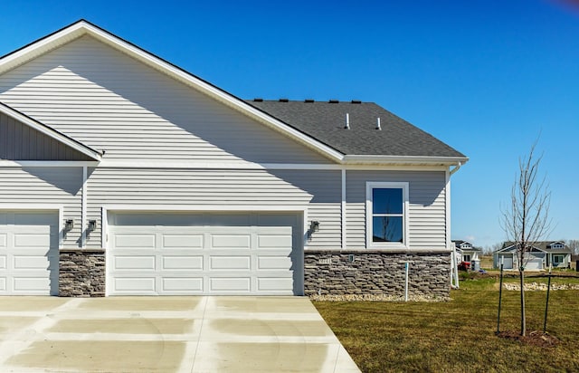 view of property exterior featuring a lawn, stone siding, and concrete driveway