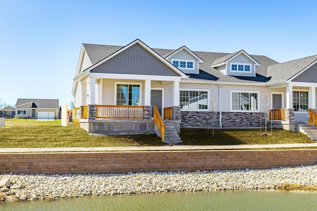 craftsman-style home with stone siding, a porch, a front yard, and a water view