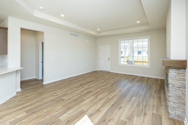 unfurnished living room featuring light wood-style flooring, a raised ceiling, baseboards, visible vents, and recessed lighting