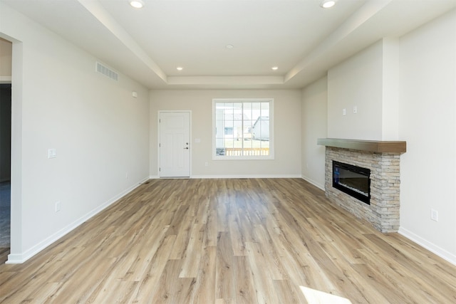 unfurnished living room featuring a fireplace, recessed lighting, a tray ceiling, and light wood-style flooring