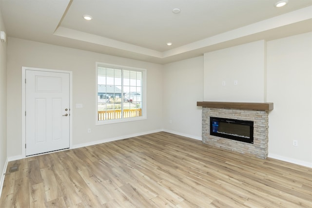 unfurnished living room with baseboards, a tray ceiling, and light wood finished floors