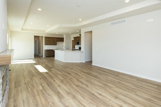 unfurnished living room with recessed lighting, light wood-style floors, visible vents, and a raised ceiling