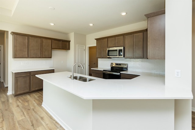 kitchen featuring tasteful backsplash, a sink, light wood-type flooring, stainless steel appliances, and light countertops