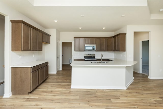 kitchen featuring light wood finished floors, a sink, appliances with stainless steel finishes, and tasteful backsplash