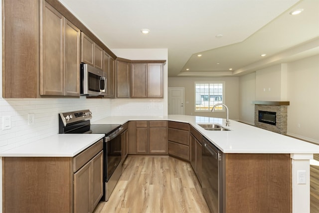 kitchen with stainless steel appliances, a sink, light wood-type flooring, a peninsula, and open floor plan