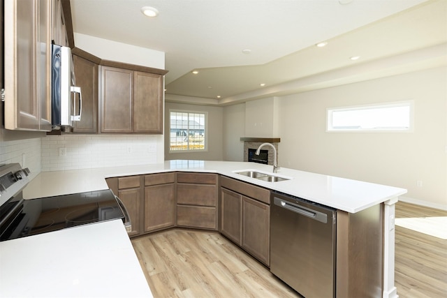 kitchen featuring light wood-type flooring, stainless steel appliances, a peninsula, and a sink