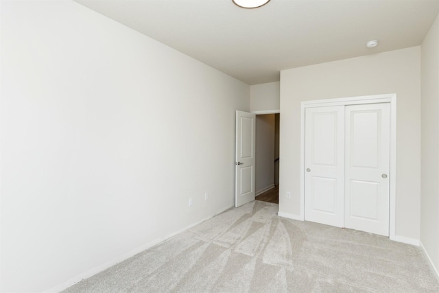 unfurnished bedroom with baseboards, light carpet, and a closet