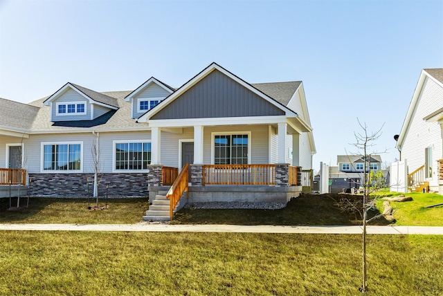 view of front facade featuring a front lawn, stone siding, and covered porch