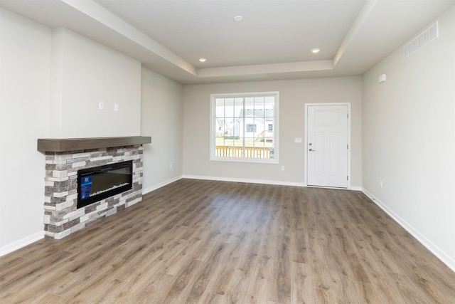 unfurnished living room featuring wood finished floors, visible vents, a stone fireplace, and a tray ceiling