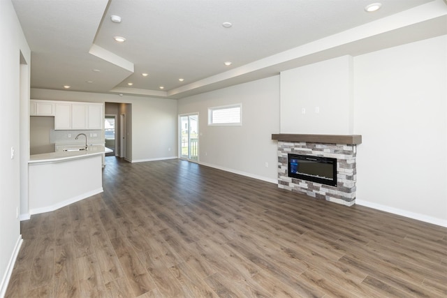 unfurnished living room featuring a tray ceiling, a sink, baseboards, recessed lighting, and wood finished floors