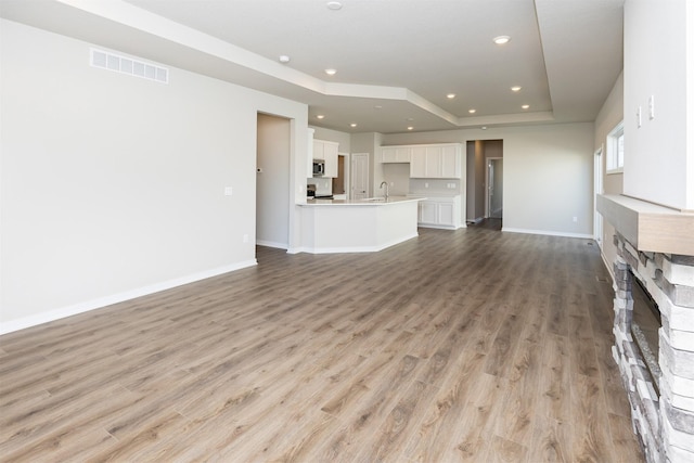 unfurnished living room featuring light wood finished floors, visible vents, recessed lighting, and a raised ceiling