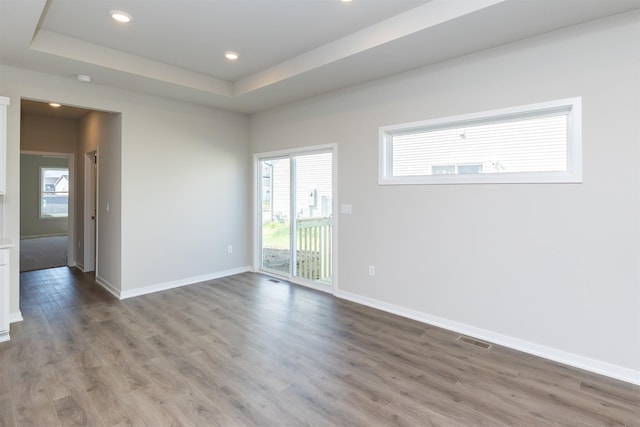 unfurnished room featuring wood finished floors, a tray ceiling, baseboards, visible vents, and recessed lighting